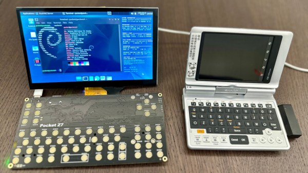 The UMPC powered up, case-less showing the black PCB, with the display standing upwards and showing a blue colour scheme desktop with a CLI terminal open. To the right of it is one of the UMPCs that served as an inspiration for this project.